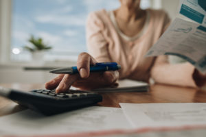 Close up of unrecognizable woman planning home budget and using calculator.